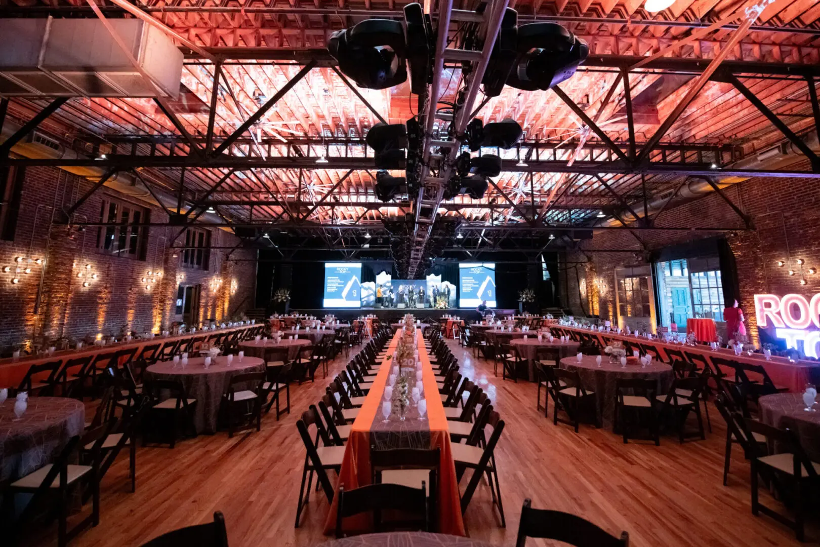 Spacious event hall with long tables and stage setup under warm lighting.