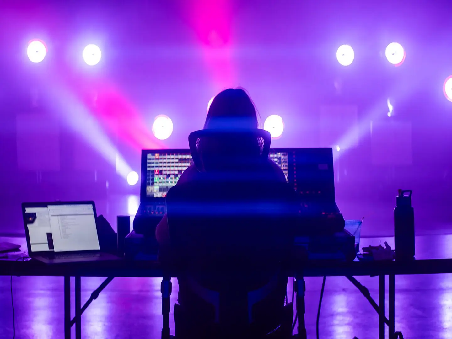 DJ performing live with vibrant purple and blue stage lighting.