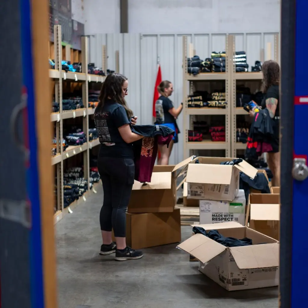 Person organizing and packing items in a storage room filled with shelves and boxes.