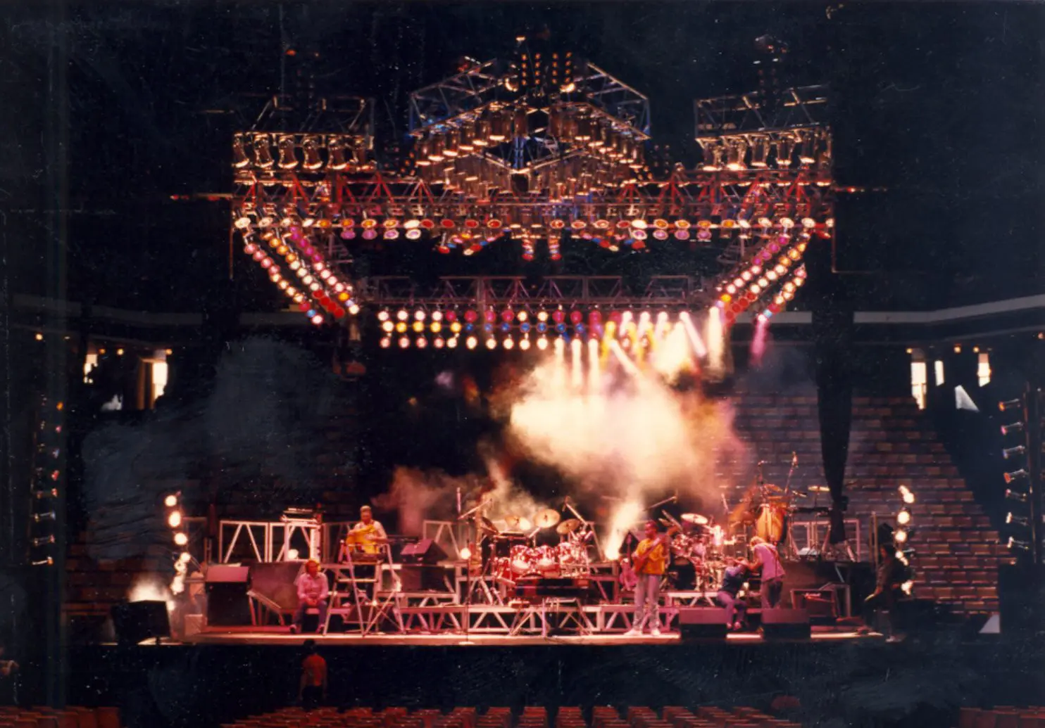 A rock band performing on a large, illuminated stage with smoke effects.