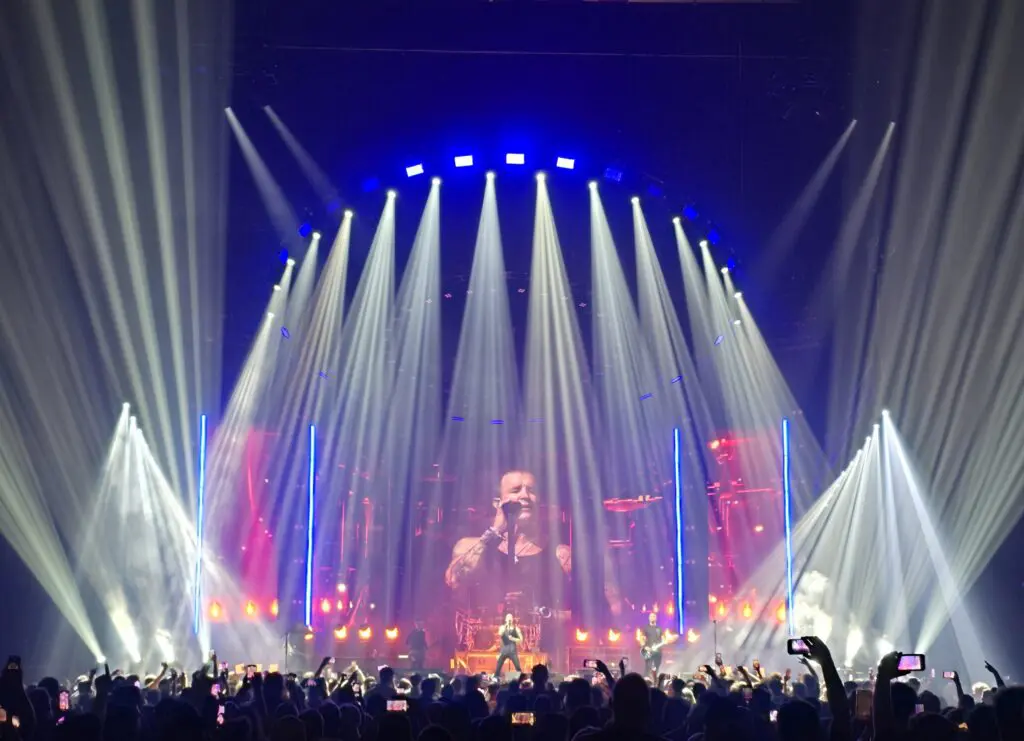 A singer performs onstage with dramatic lighting and a large crowd.