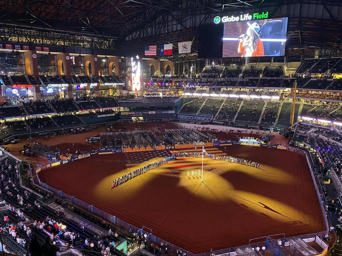 Indoor rodeo event with dirt arena and spectators in a large stadium.