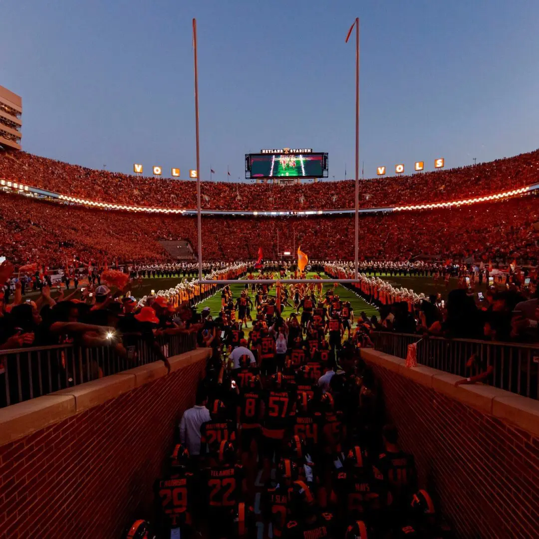 Crowded stadium during a football game with fans entering the field area.