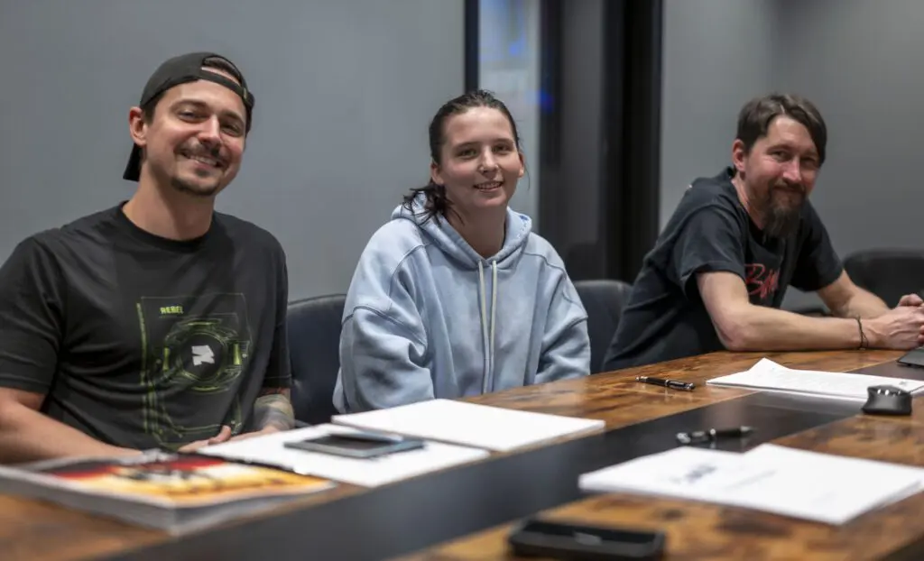 Three people smiling and sitting at a table with papers and pens.