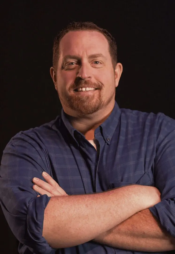 Smiling man with crossed arms wearing a blue shirt.