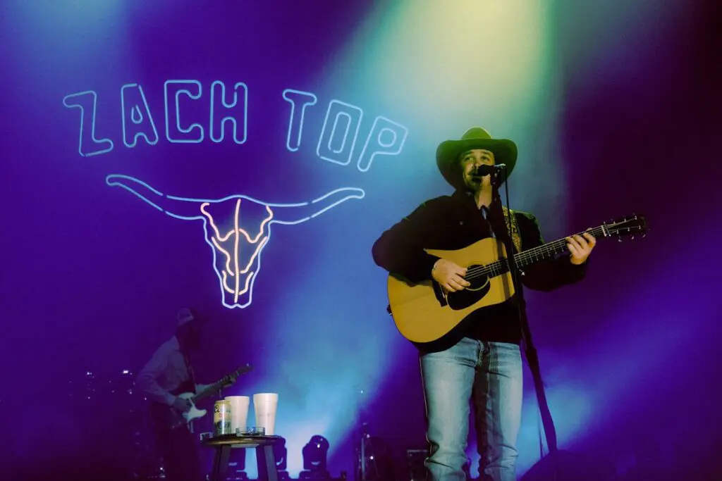 Musician playing guitar on stage under colorful lights at Peach Top.