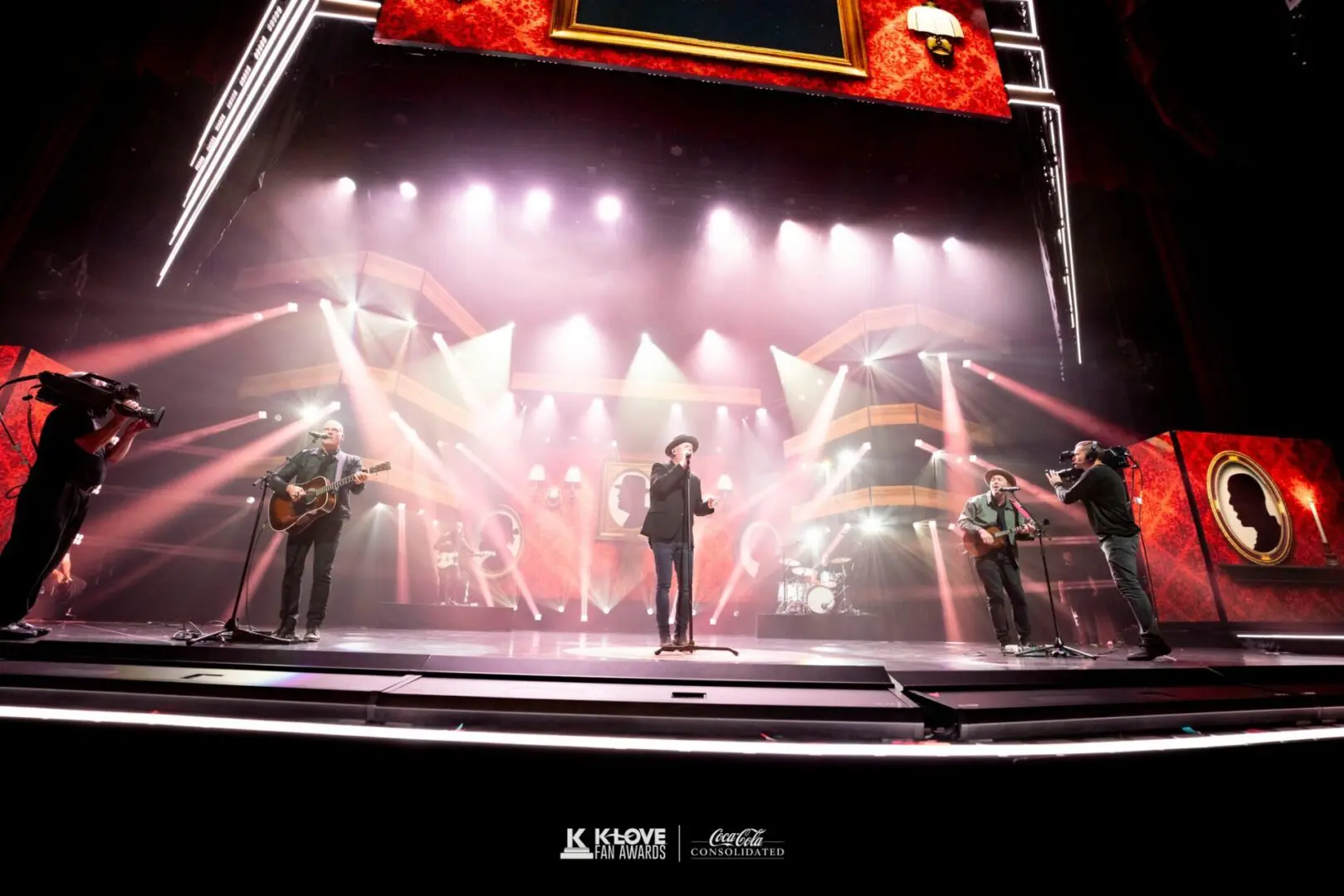 A singer performs on a brightly lit stage with a band and dramatic lighting.