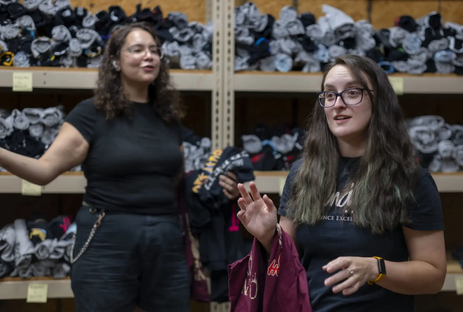 Two women discussing clothing items in a warehouse setting.