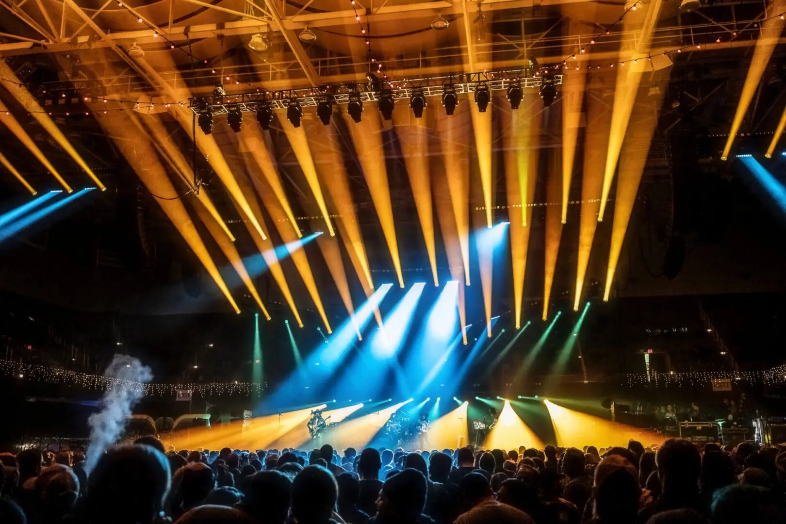 Colorful stage lights illuminate a concert with an enthusiastic crowd.