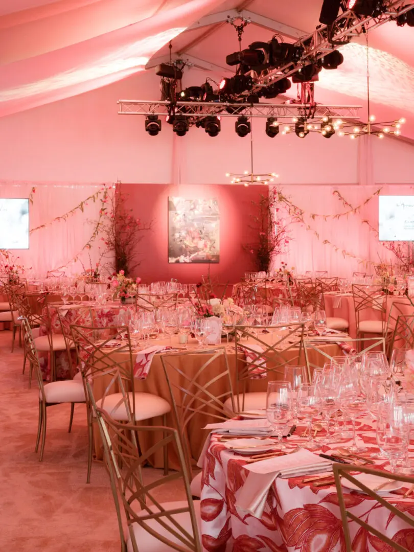Elegant wedding reception setup with round tables and soft pink lighting.
