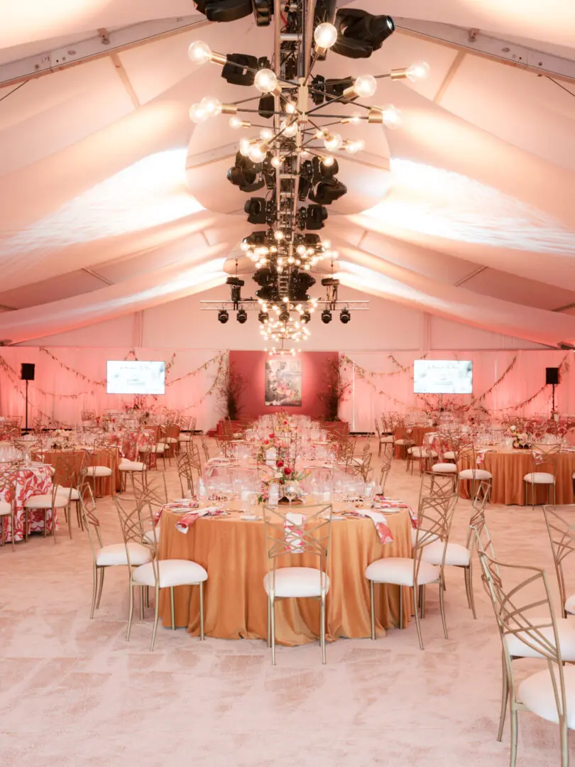 Elegant wedding reception setup with round tables and soft pink lighting.