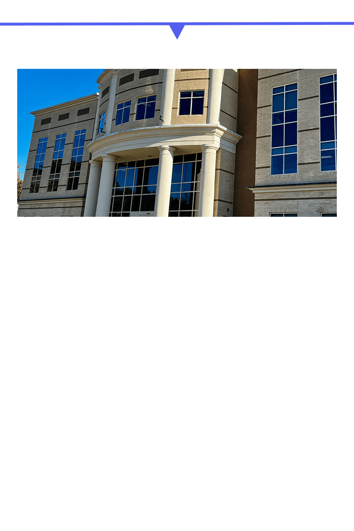 Modern stone building with large columns and windows under a clear blue sky.