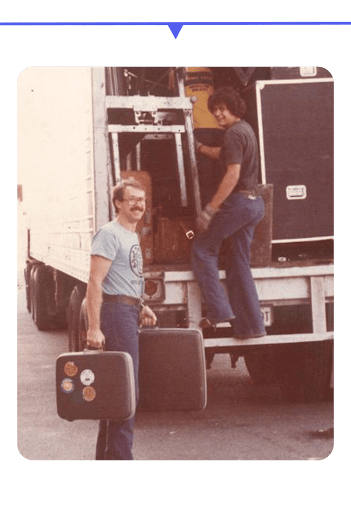 Two men carrying large dice near a truck.