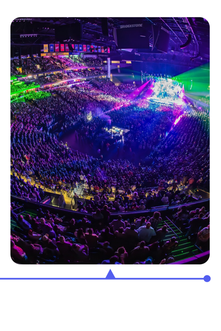 A packed arena lit with colorful lights during a concert.