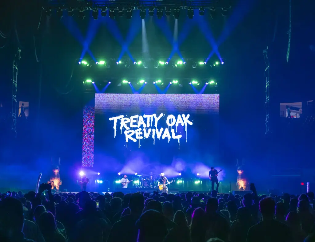A live concert with vibrant lighting and Treaty Oak Revival on the screen.