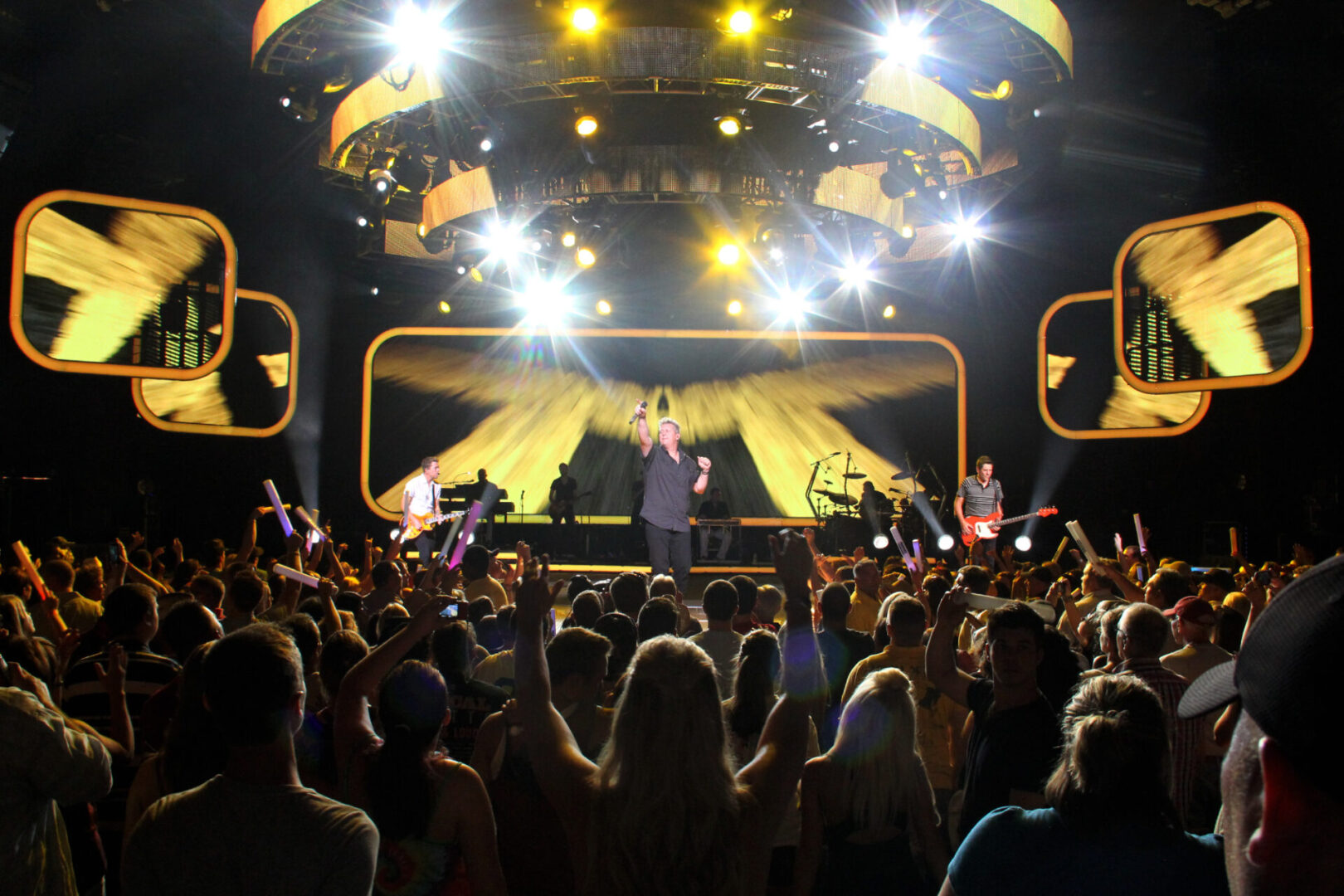 Crowd watching a performer on a brightly lit stage with yellow spotlights.