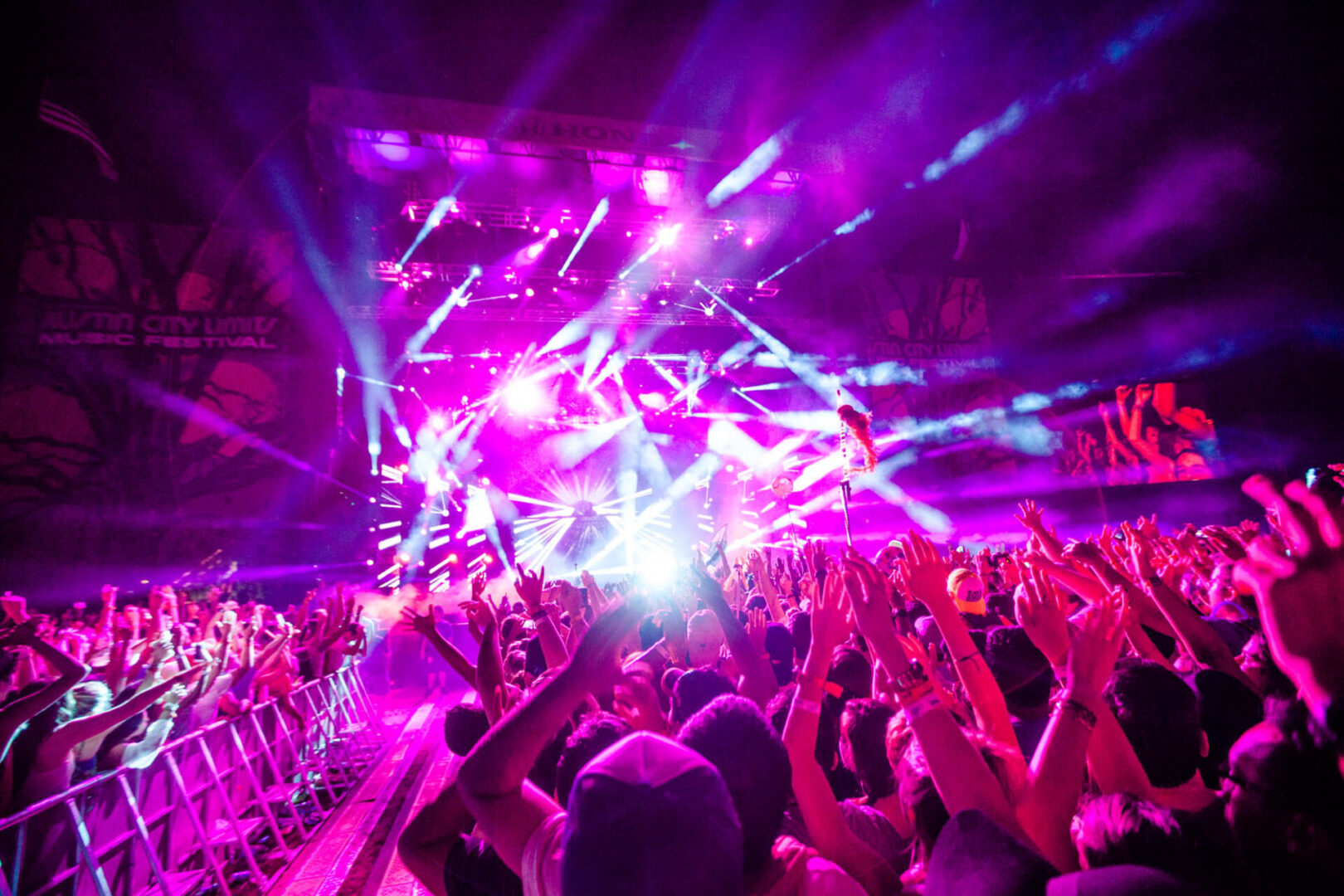 A vibrant crowd enjoying a lively concert with bright purple and pink stage lights.