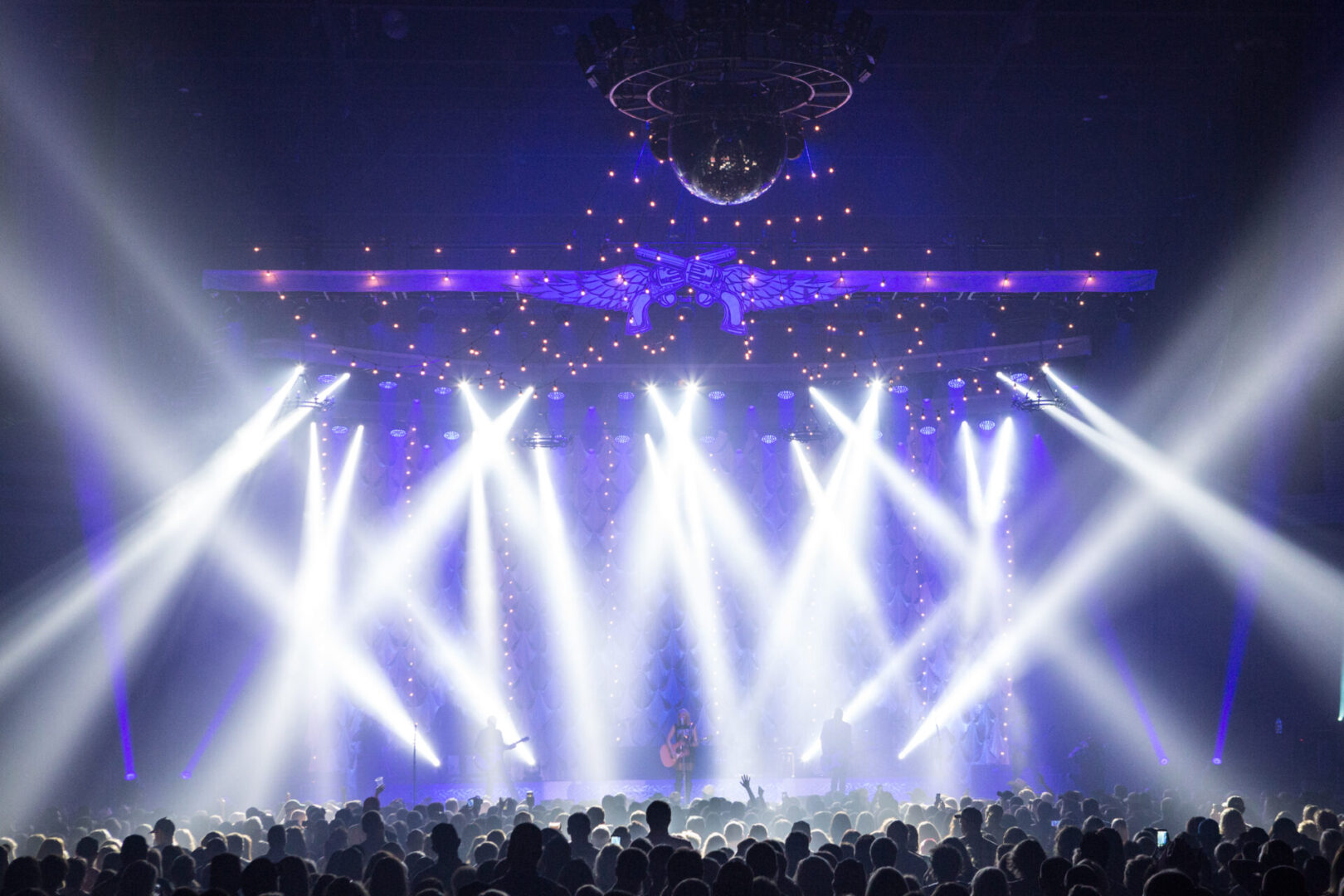 Bright white stage lights beam over a packed concert crowd.