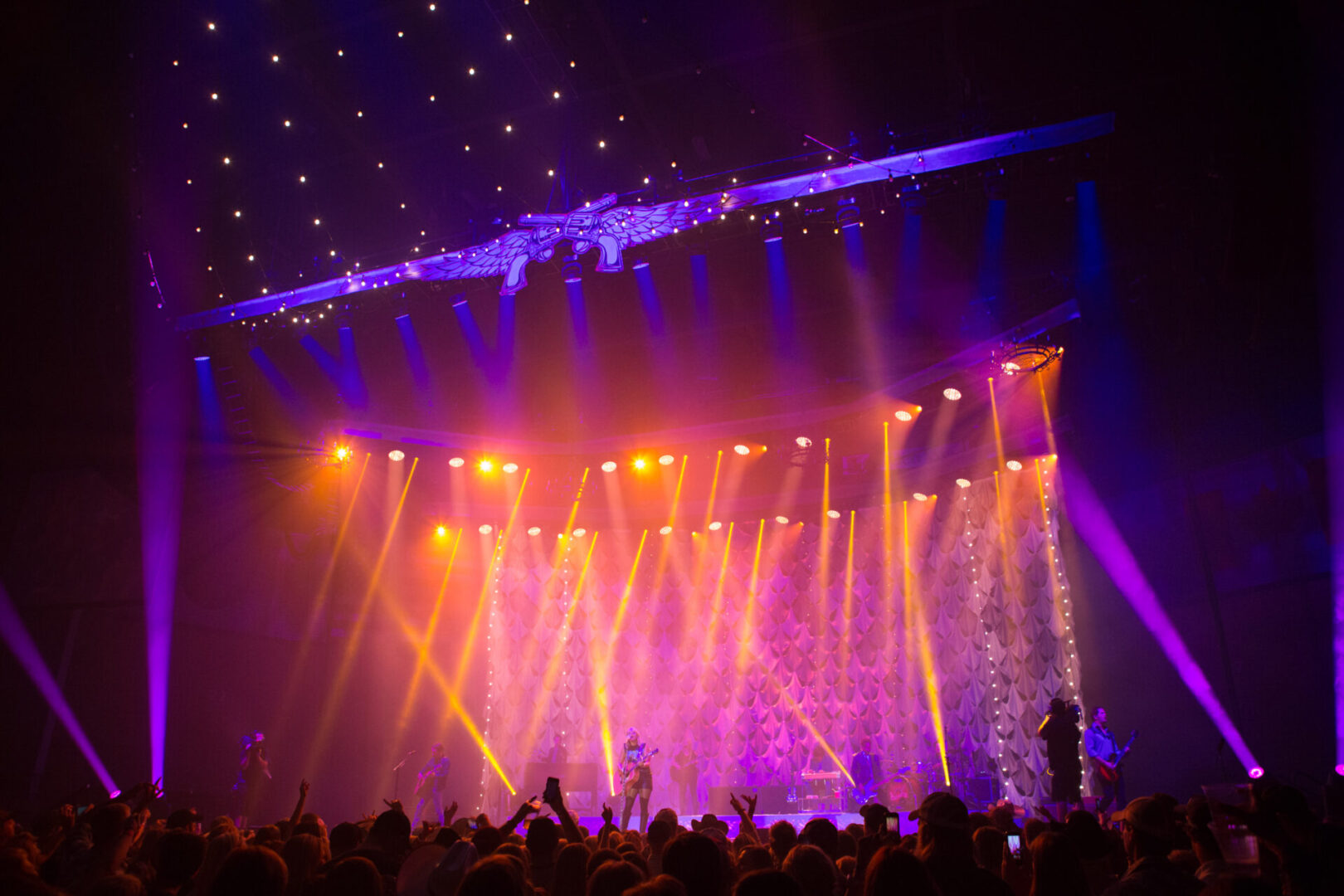 Colorful stage lights illuminate a concert with a lively audience.