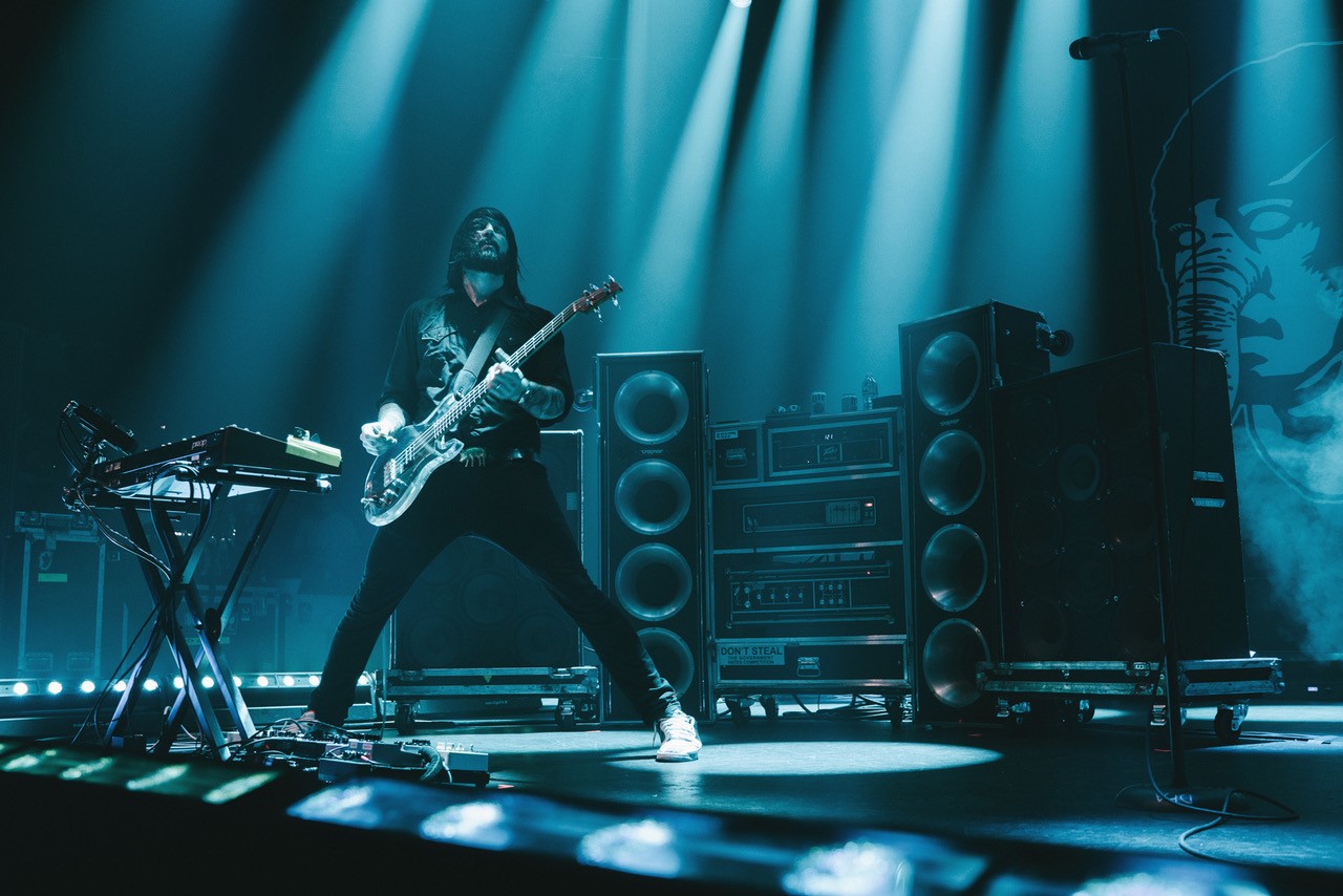 Guitarist performing energetically on stage with dramatic blue lighting.