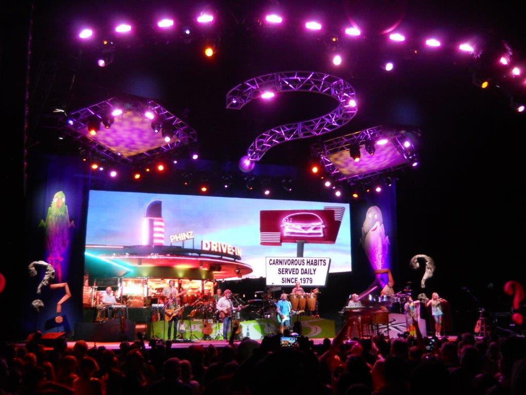 A vibrant nighttime concert with colorful lights and a large screen.