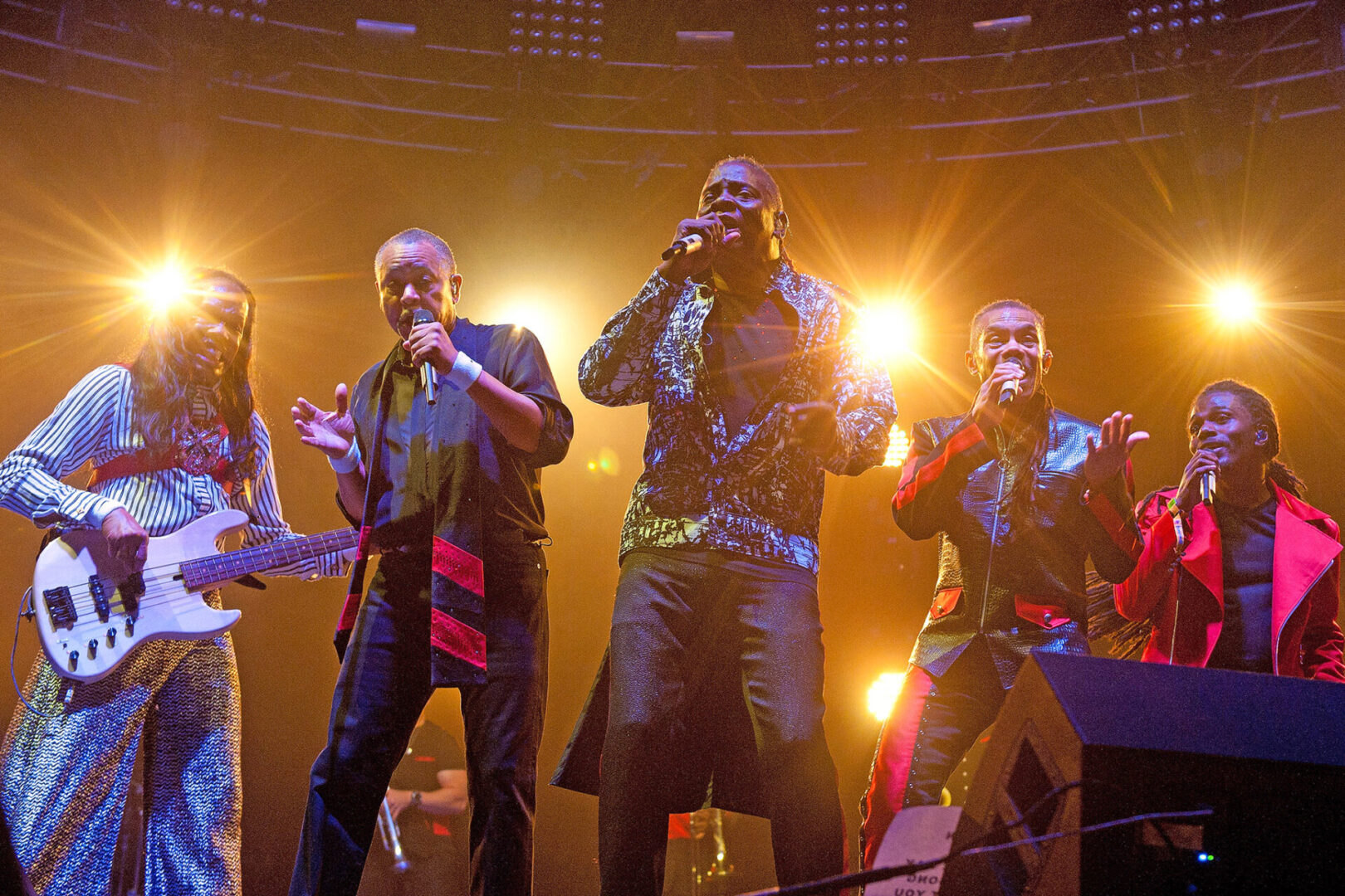 A vibrant band performs energetically on stage with colorful lighting.