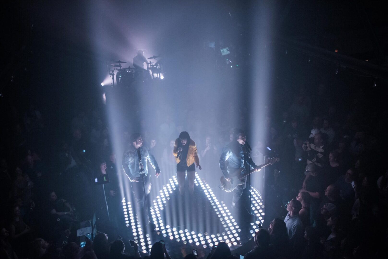 A singer performs under dramatic spotlight beams on stage with backup dancers.