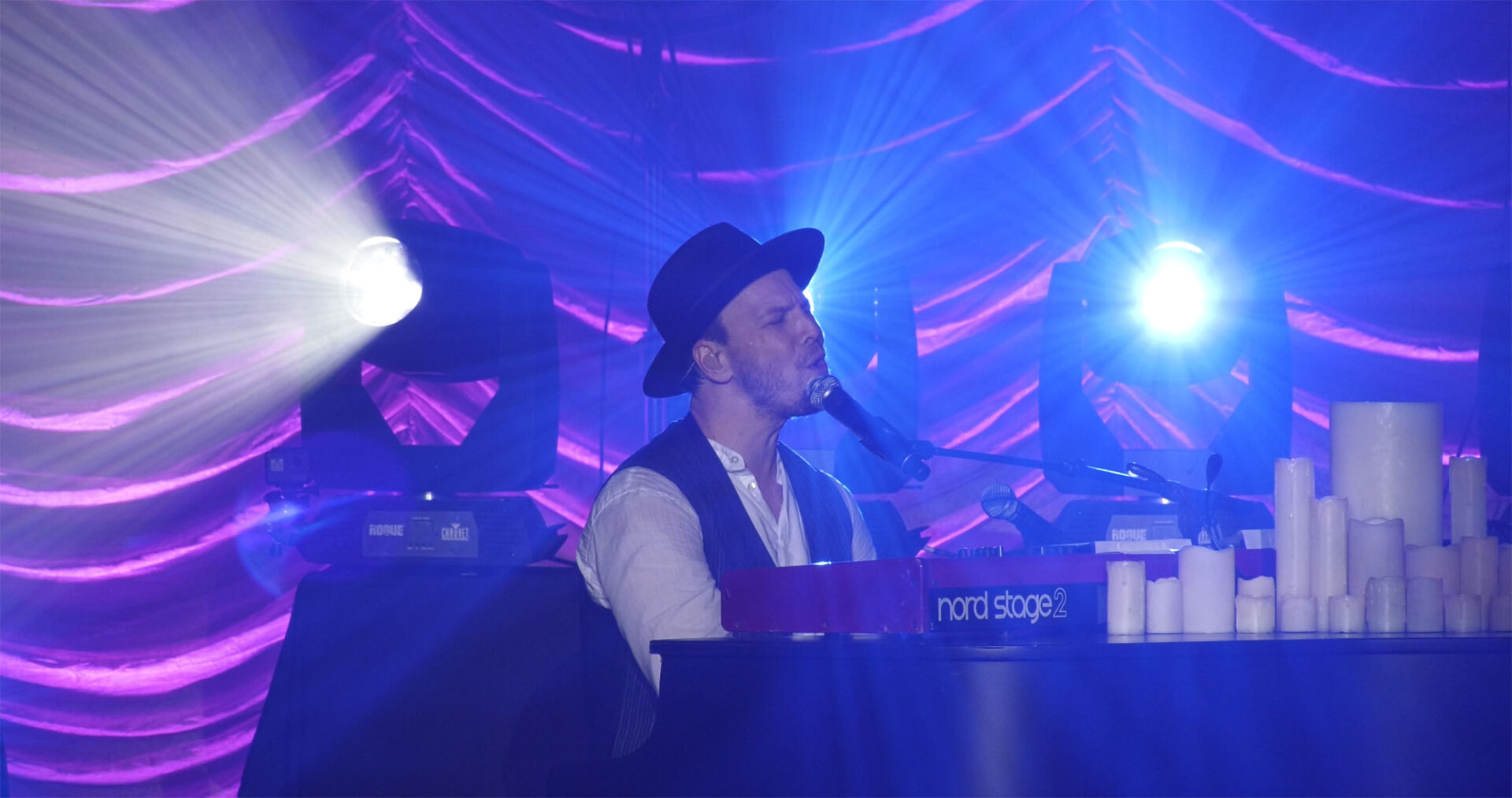 A musician plays keyboard on stage under blue and purple lights.