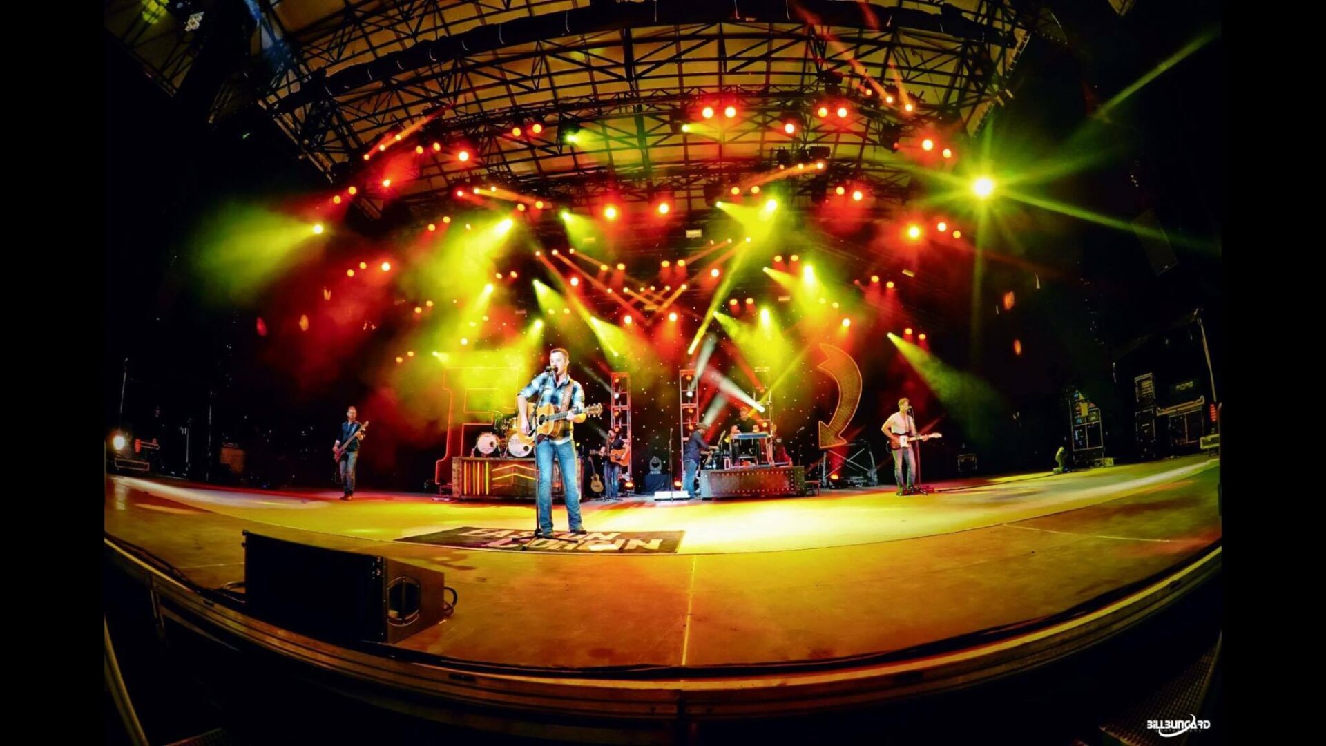 Band performing live on a brightly lit stage with colorful lights.