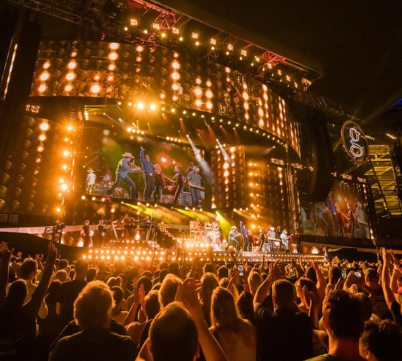 Crowd enjoying a brightly lit outdoor concert at night.