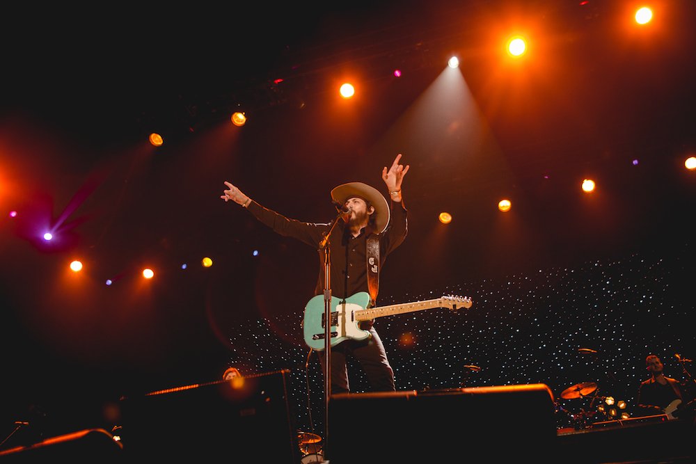 Musician passionately performing on stage with guitar under bright lights.