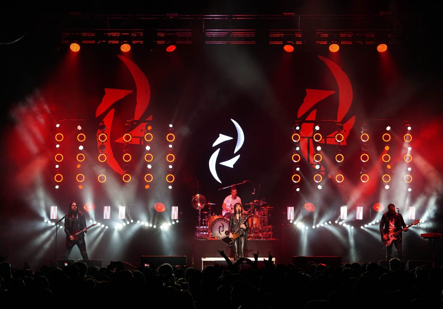 A band performing on stage with dramatic red lighting and a large logo backdrop.