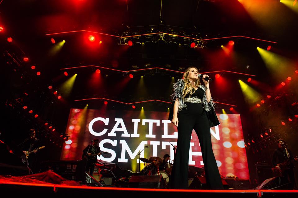 Caitlin Smith performing live on stage with vibrant red lighting.