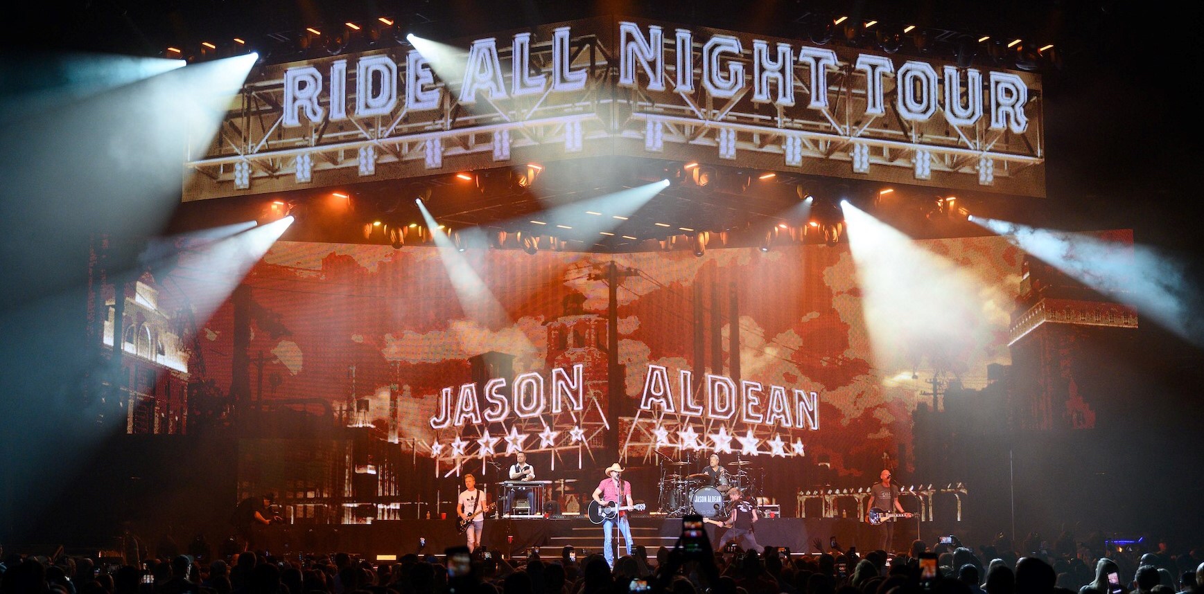 Jason Aldean performing live on stage with vibrant lighting.