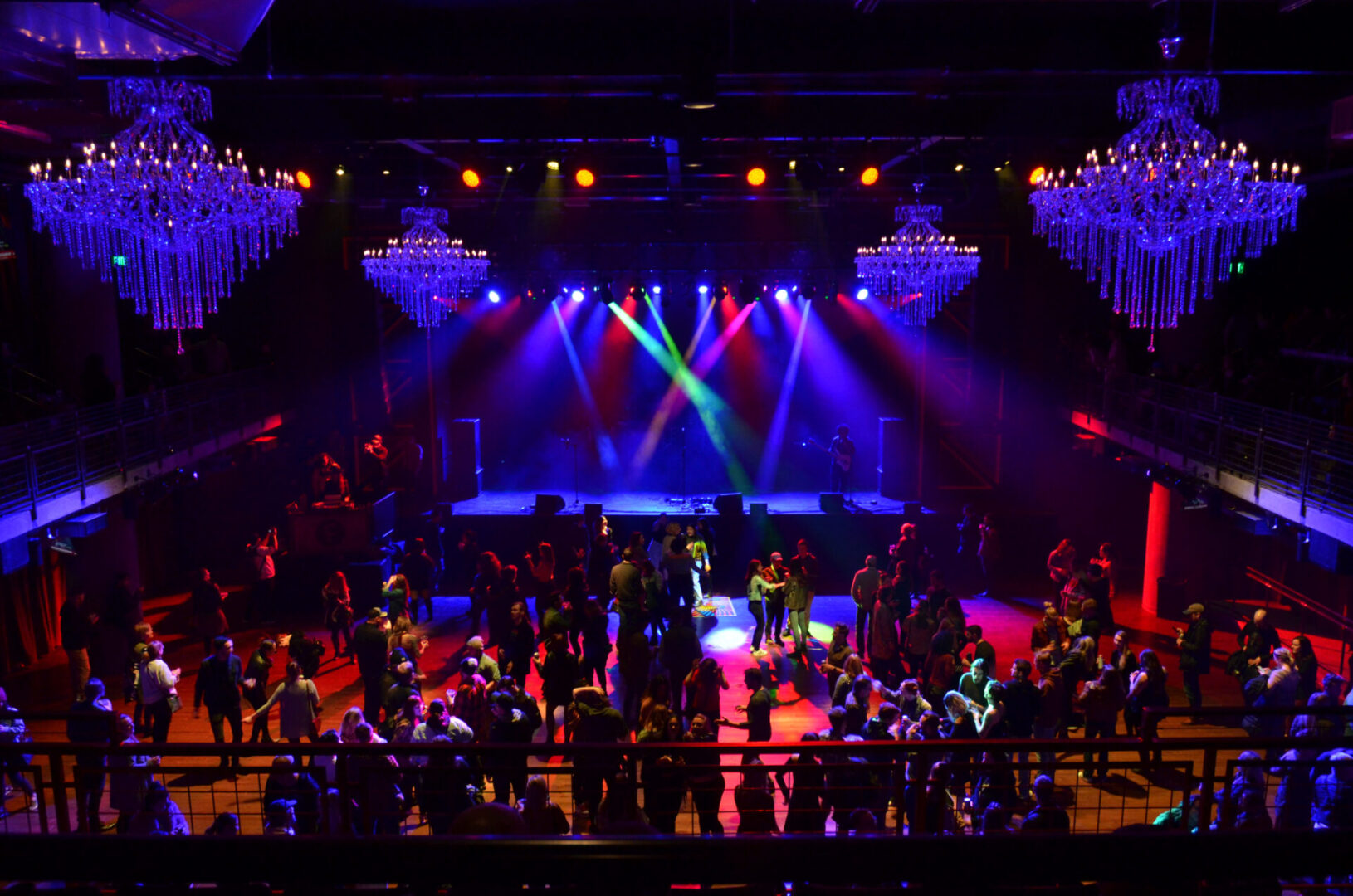 Colorful stage lights illuminate a lively concert crowd in a grand venue.