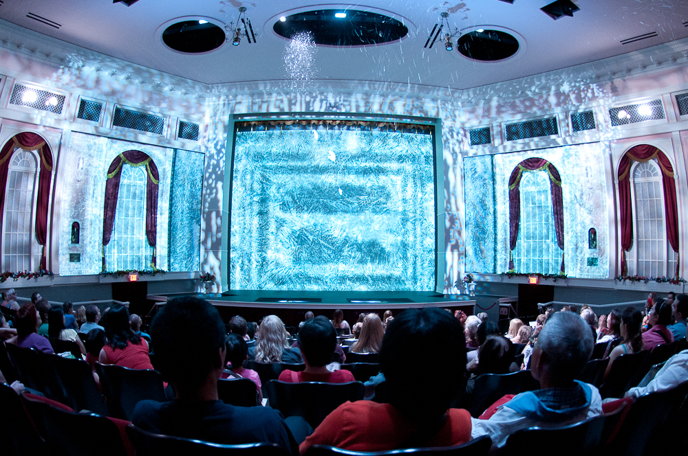 Audience watching a theater show with a blue-hued stage.