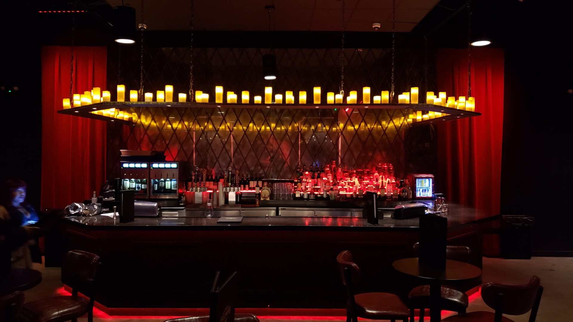 Dimly lit bar with rows of candles and red ambient lighting.