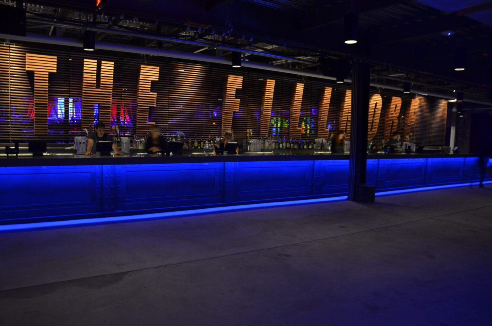 A dimly lit bar with blue LED lighting under the counter and bottles displayed on shelves.