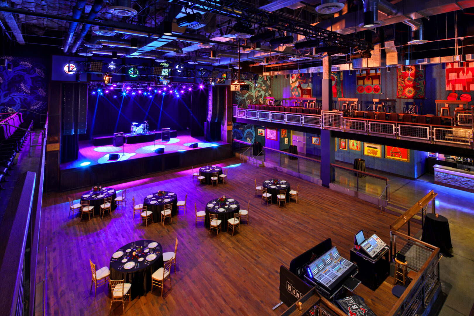 Spacious venue with stage and dining tables under colorful lights.