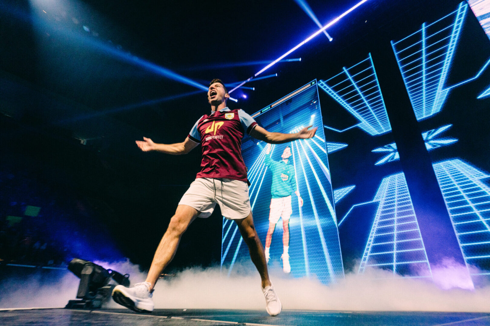 Energetic performer jumping on stage with vibrant blue lights and smoke effects.