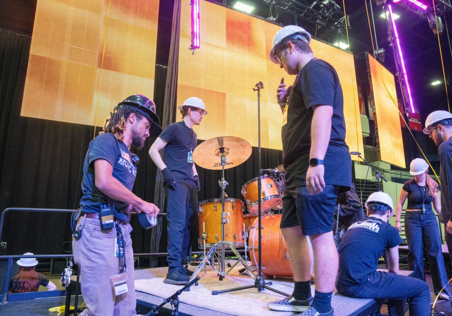 People setting up drums on a stage with bright lights.