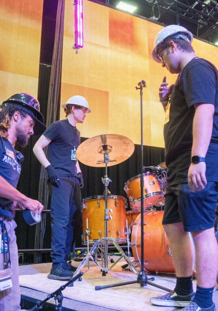 People setting up drums on a stage with bright lights.