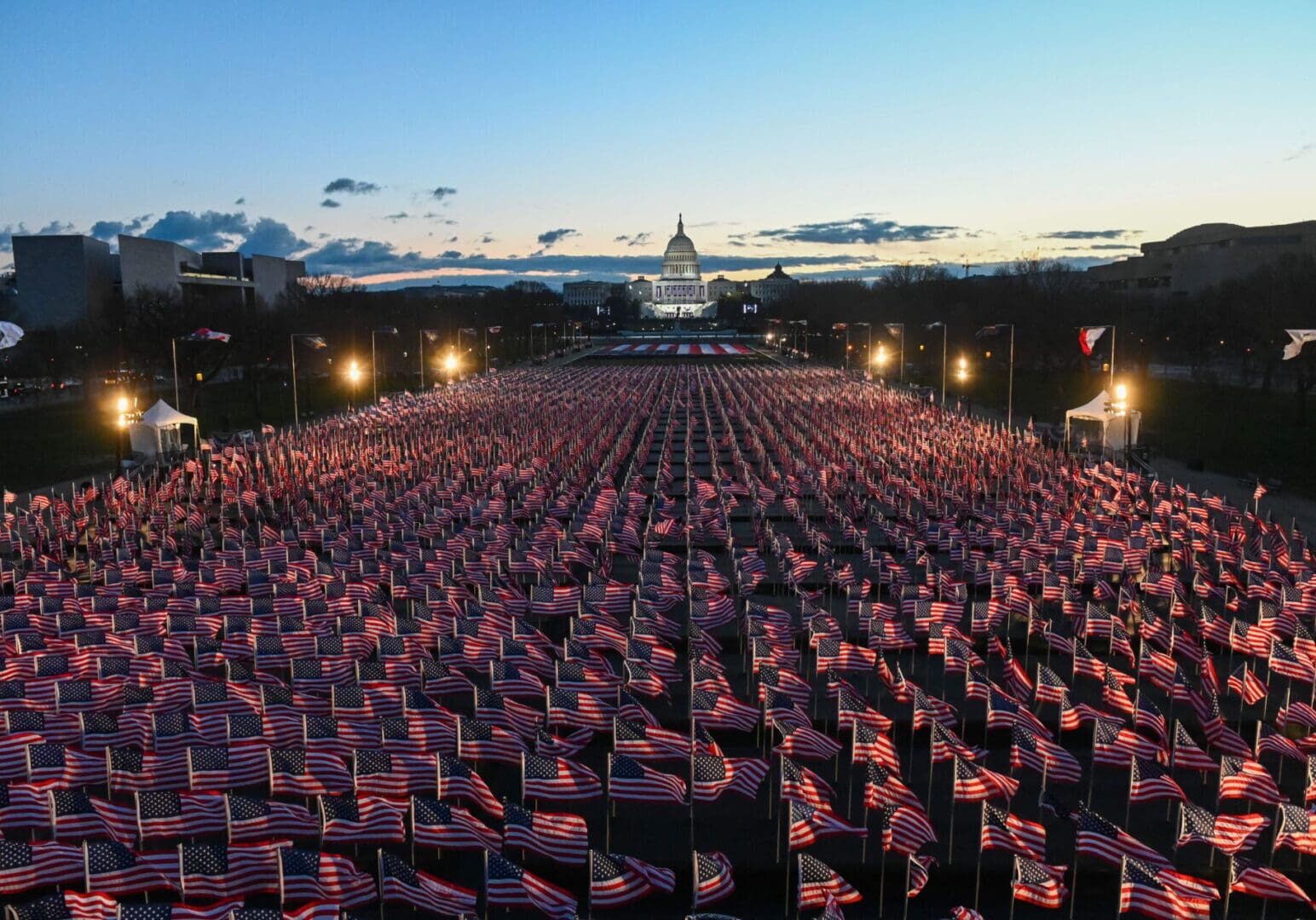 Large crowd waving American flags at dusk near Capitol building.