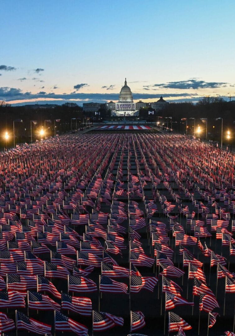 Large crowd waving American flags at dusk near Capitol building.