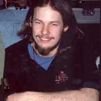 A man with long hair and a beard smiling indoors.