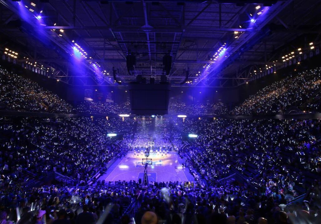 A packed arena with purple lighting during a live event.
