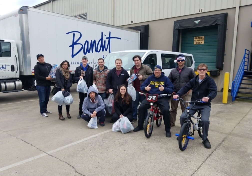 Group photo of cheerful people outside a Bandit-branded vehicle.