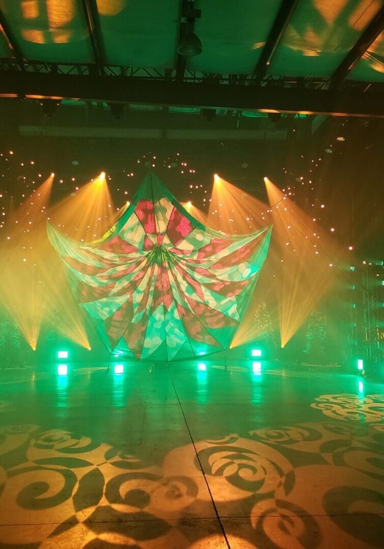 Colorful stage lights and geometric projections create a vibrant atmosphere.