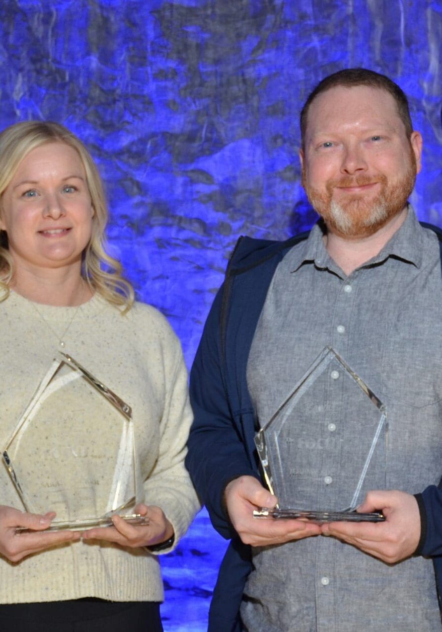 Two people holding awards, smiling at a formal event with blue lighting.