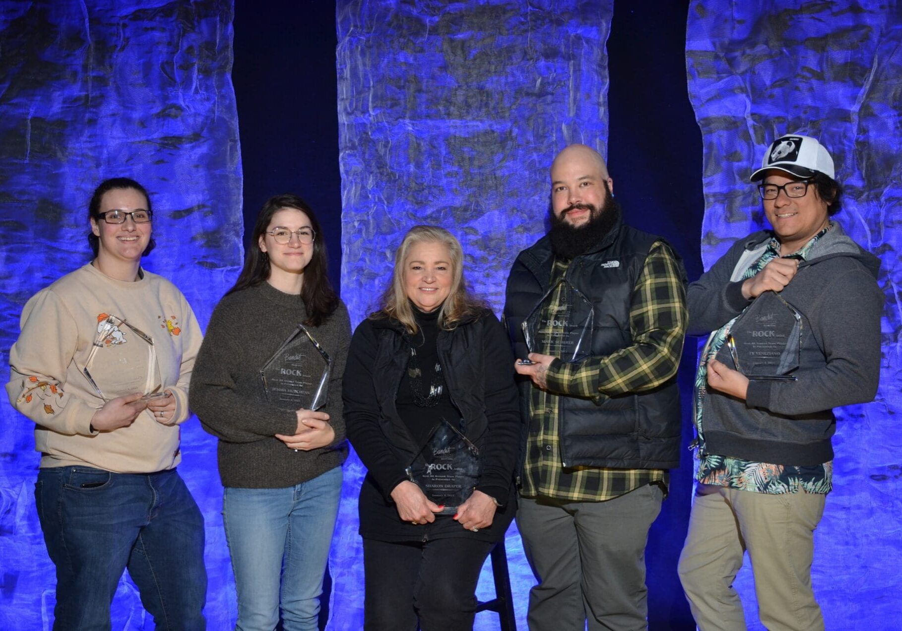 Five people posing together against a stone wall with blue lighting.